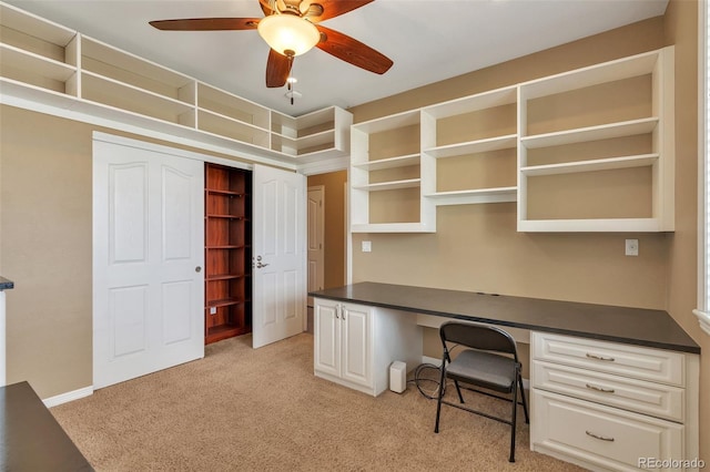 unfurnished office with light colored carpet, built in desk, baseboards, and ceiling fan