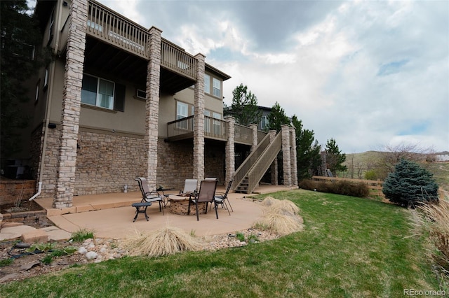back of house featuring stone siding, stucco siding, a patio area, a yard, and a fire pit
