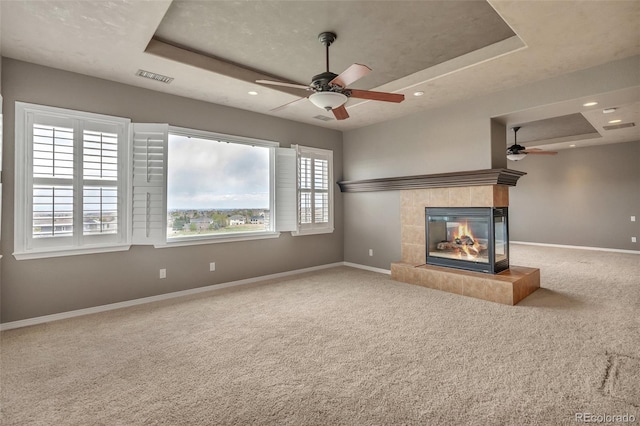 unfurnished living room with a ceiling fan, visible vents, baseboards, carpet, and a tray ceiling