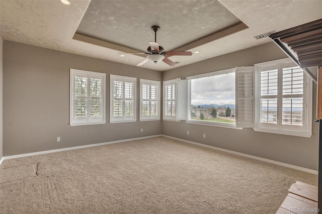 empty room featuring visible vents, baseboards, ceiling fan, a raised ceiling, and carpet flooring