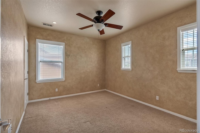 carpeted empty room featuring a ceiling fan, a textured wall, visible vents, and baseboards