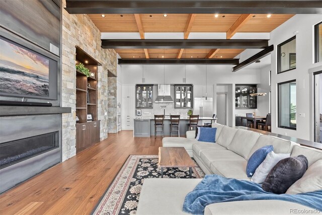 living room featuring built in shelves, a stone fireplace, wood ceiling, and hardwood / wood-style floors