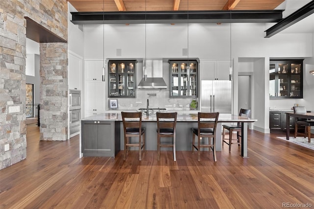 kitchen with appliances with stainless steel finishes, wall chimney exhaust hood, a towering ceiling, and dark hardwood / wood-style floors