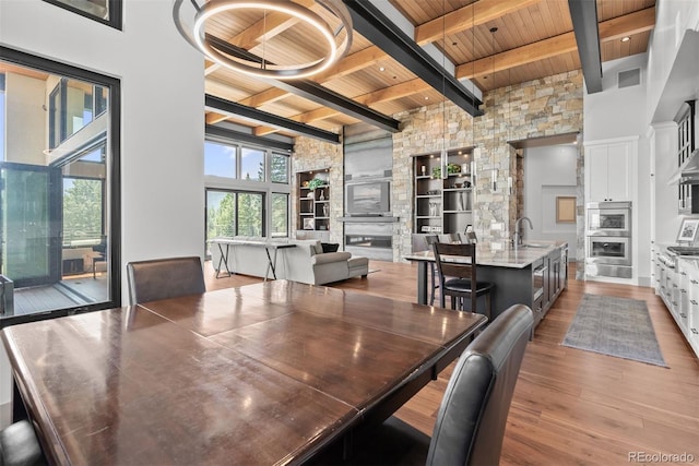 dining area featuring a towering ceiling, a fireplace, wooden ceiling, wood-type flooring, and beam ceiling