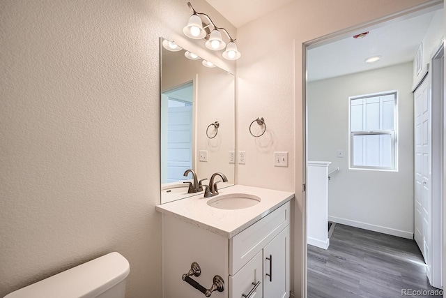 bathroom with vanity, wood finished floors, baseboards, toilet, and a textured wall