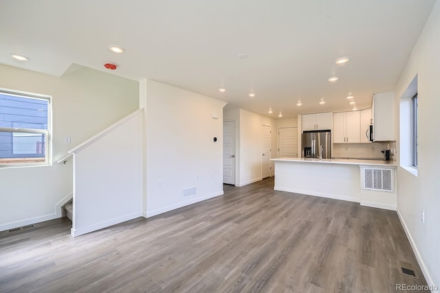 kitchen with white cabinets, light hardwood / wood-style flooring, tasteful backsplash, kitchen peninsula, and stainless steel appliances