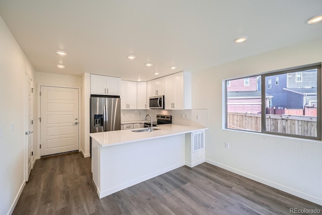 kitchen with a peninsula, a sink, stainless steel appliances, light countertops, and white cabinetry