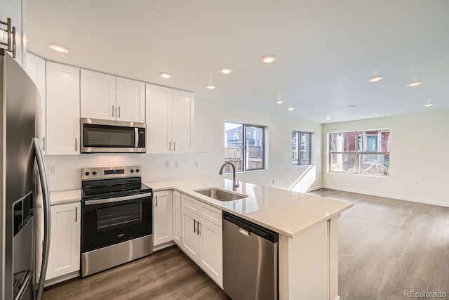 kitchen with dark wood finished floors, decorative backsplash, appliances with stainless steel finishes, a peninsula, and a sink