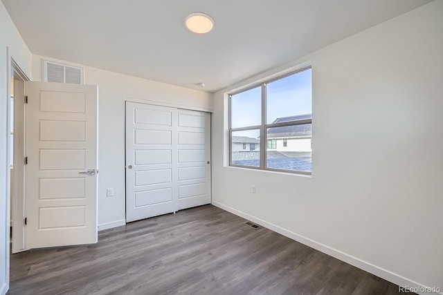 unfurnished bedroom featuring visible vents, baseboards, a closet, and wood finished floors