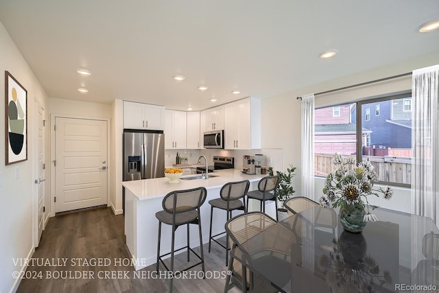 kitchen with light countertops, appliances with stainless steel finishes, a peninsula, white cabinetry, and a sink