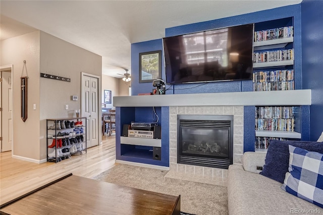 living room with built in features, hardwood / wood-style floors, ceiling fan, and a tiled fireplace