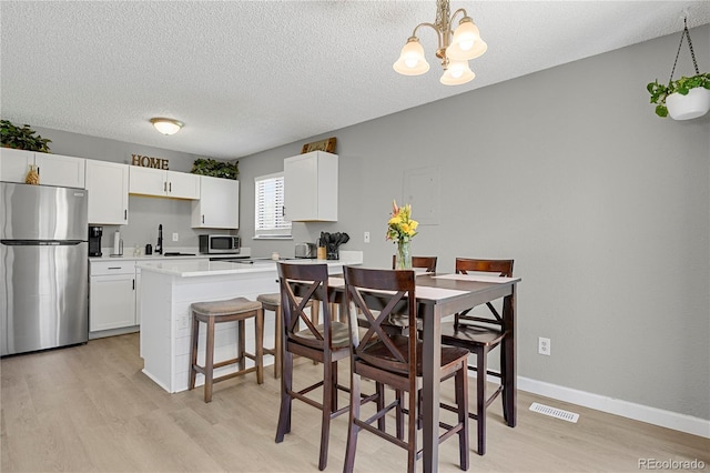 2185 Ambleside Dr, Colorado Springs, CO 80915 - dining area with light wood-style flooring, a chandelier, a textured ceiling, and baseboards