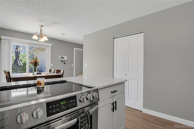 2185 Ambleside Dr, Colorado Springs, CO 80915 - kitchen featuring electric stove, a chandelier, light wood-style flooring, a textured ceiling, and baseboards