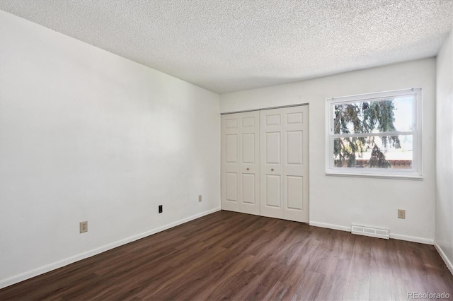 unfurnished bedroom featuring a textured ceiling, a closet, and dark hardwood / wood-style flooring