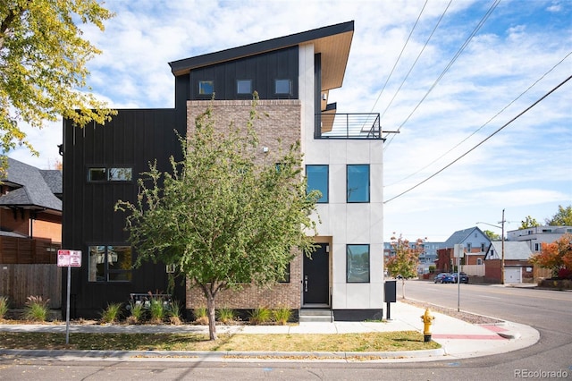 contemporary house featuring a balcony, brick siding, and board and batten siding