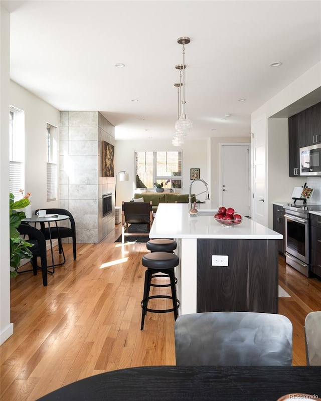 kitchen featuring a center island with sink, a tiled fireplace, appliances with stainless steel finishes, light wood finished floors, and light countertops