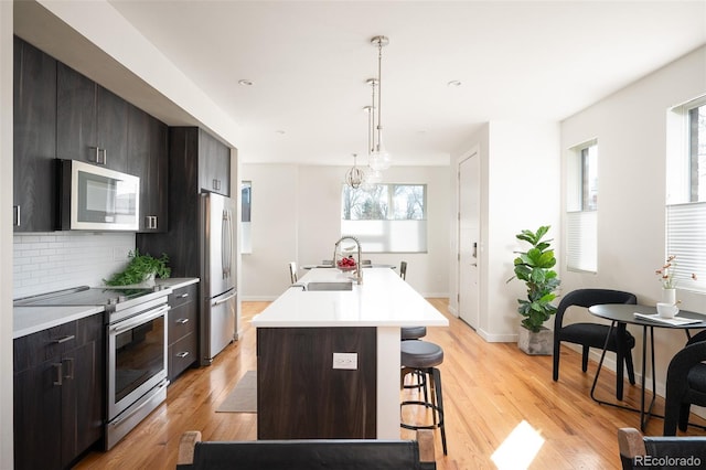 kitchen featuring a breakfast bar area, stainless steel appliances, light wood-style floors, and a sink