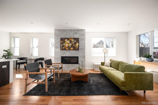 living area featuring plenty of natural light, wood finished floors, baseboards, and a tile fireplace