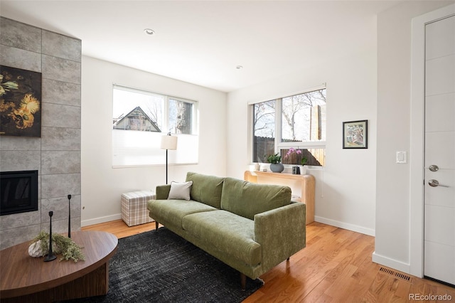 living area with visible vents, baseboards, light wood-style flooring, and a tile fireplace