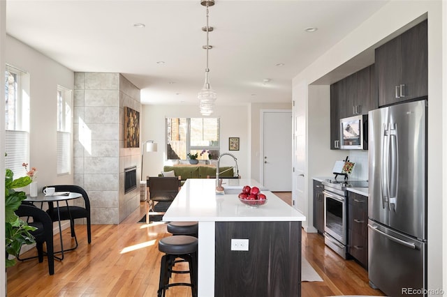 kitchen with light wood-type flooring, a kitchen bar, stainless steel appliances, a fireplace, and light countertops