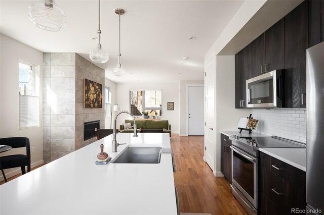 kitchen with light countertops, appliances with stainless steel finishes, a fireplace, wood finished floors, and a sink