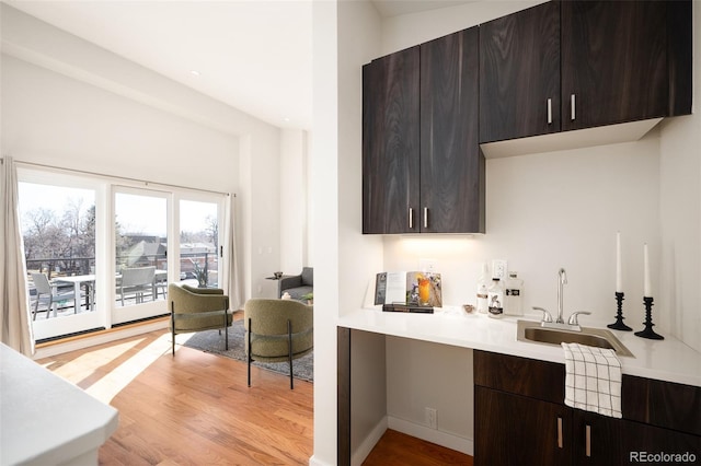 kitchen featuring light countertops, light wood-style flooring, dark brown cabinets, and a sink