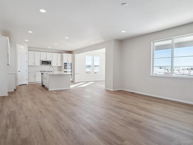 kitchen featuring white cabinets, appliances with stainless steel finishes, light hardwood / wood-style floors, and an island with sink