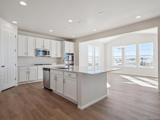 kitchen featuring a kitchen island with sink, white cabinets, hanging light fixtures, light hardwood / wood-style floors, and stainless steel appliances