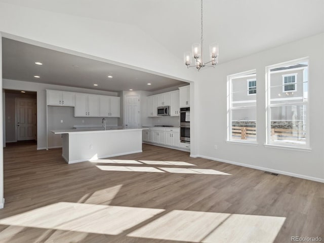 kitchen featuring pendant lighting, a kitchen island with sink, white cabinets, vaulted ceiling, and appliances with stainless steel finishes