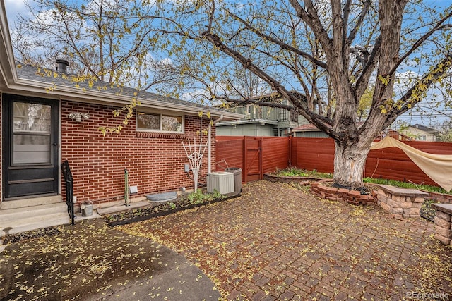 view of side of property featuring cooling unit, a fenced backyard, brick siding, a patio area, and entry steps