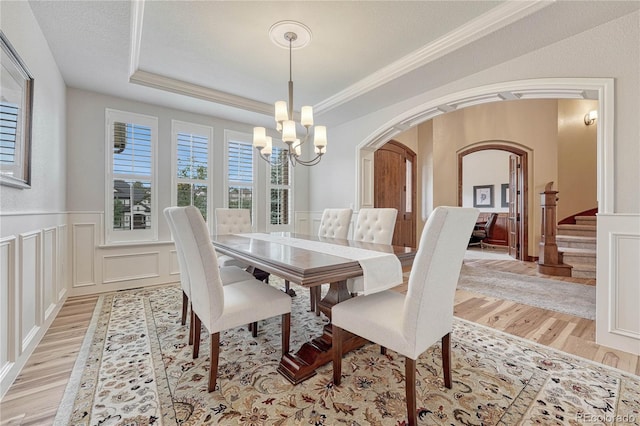 9121 Sunshine Meadow Pl, Parker, CO 80134 - dining area with arched walkways, a chandelier, light wood-style floors, a decorative wall, and wainscoting