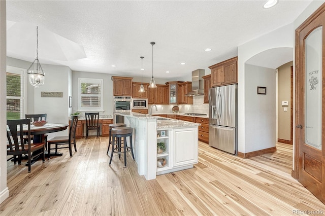 9121 Sunshine Meadow Pl, Parker, CO 80134 - kitchen featuring appliances with stainless steel finishes, wall chimney exhaust hood, a sink, brown cabinets, and arched walkways
