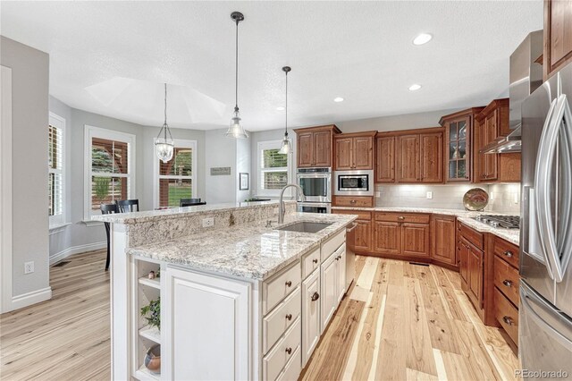 9121 Sunshine Meadow Pl, Parker, CO 80134 - kitchen with stainless steel appliances, light wood-style floors, brown cabinets, open shelves, and an island with sink