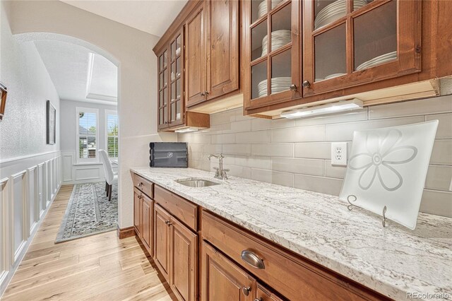9121 Sunshine Meadow Pl, Parker, CO 80134 - kitchen featuring a sink, arched walkways, light wood-style floors, light stone countertops, and brown cabinets