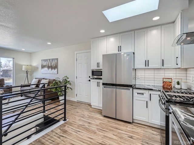 kitchen with light wood finished floors, wall chimney exhaust hood, open floor plan, stainless steel appliances, and white cabinetry