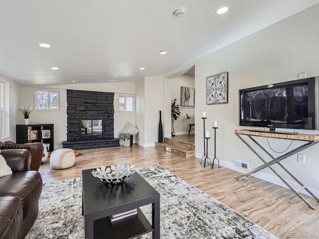 living area featuring baseboards, visible vents, wood finished floors, vaulted ceiling, and a stone fireplace