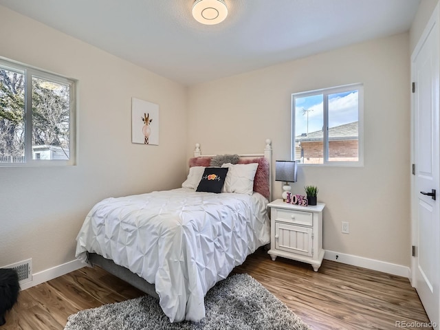 bedroom with baseboards, visible vents, and wood finished floors