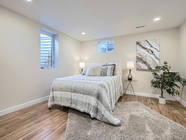 bedroom featuring baseboards, multiple windows, visible vents, and wood finished floors