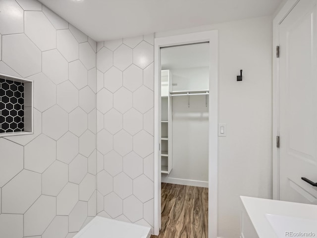 bathroom featuring a sink, a spacious closet, tiled shower, and wood finished floors