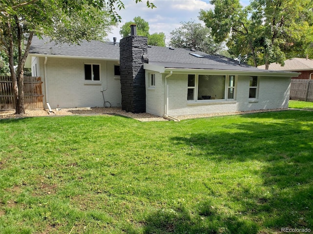 rear view of property with brick siding, a chimney, fence, and a lawn