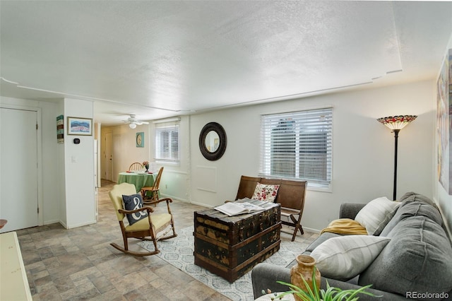 living area featuring stone finish floor, a ceiling fan, baseboards, and a textured ceiling