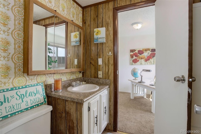 half bathroom with toilet, a textured ceiling, wallpapered walls, and vanity