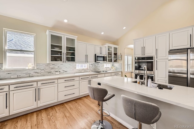 kitchen with arched walkways, lofted ceiling, appliances with stainless steel finishes, a kitchen bar, and white cabinetry