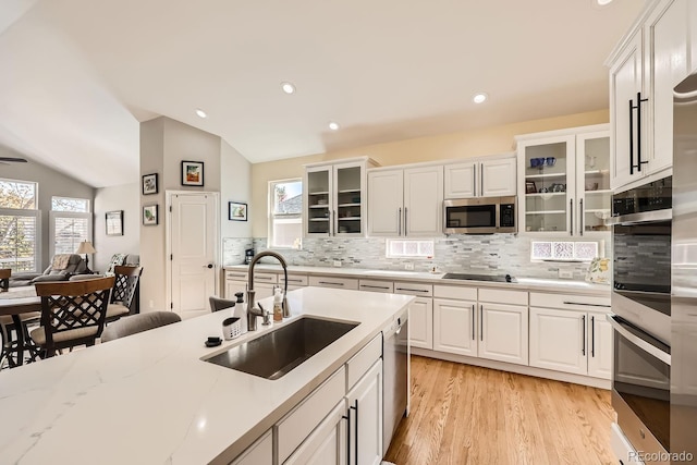 kitchen with lofted ceiling, white cabinetry, stainless steel appliances, and a sink