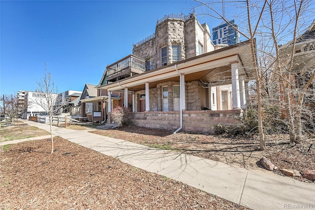 view of front of property featuring stone siding, a balcony, and a porch