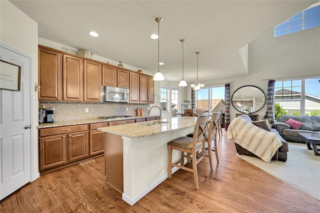 5722 S Flat Rock Way, Aurora, CO 80016 - kitchen featuring appliances with stainless steel finishes, open floor plan, light wood finished floors, brown cabinetry, and a breakfast bar area