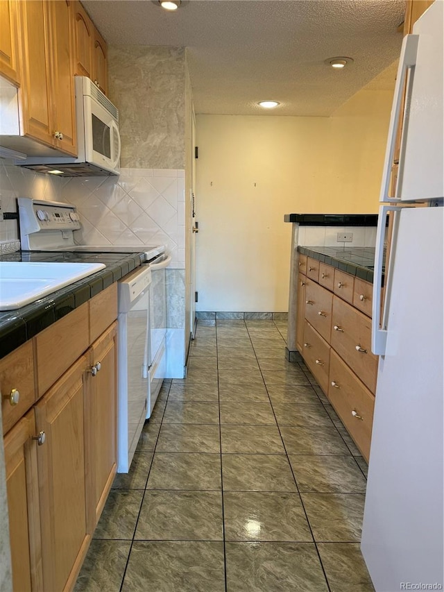 kitchen featuring tile counters, tasteful backsplash, a textured ceiling, white appliances, and dark tile patterned flooring