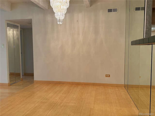 spare room featuring a chandelier and light hardwood / wood-style flooring