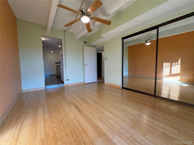 unfurnished bedroom with beam ceiling, a closet, light hardwood / wood-style flooring, and a textured ceiling