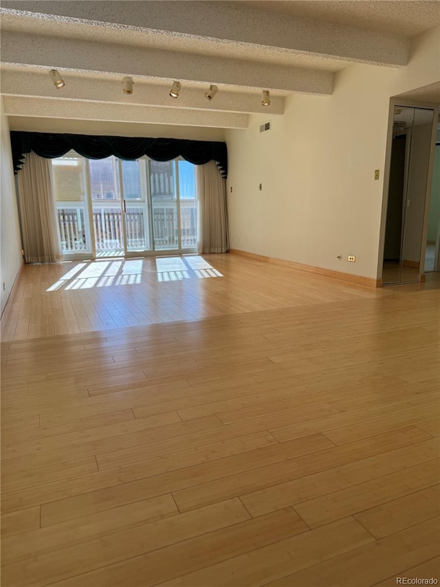 spare room featuring light hardwood / wood-style flooring, beamed ceiling, a healthy amount of sunlight, and a textured ceiling